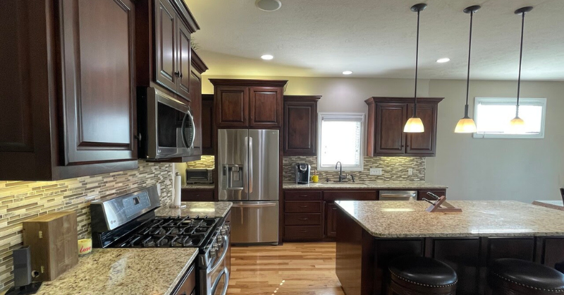 Kitchen with brown toned cabinets, golden floors, and stainless steel appliances.