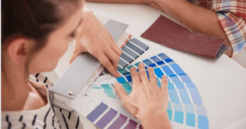 Person looking at blue and purple paint swatch sticks on a desk.