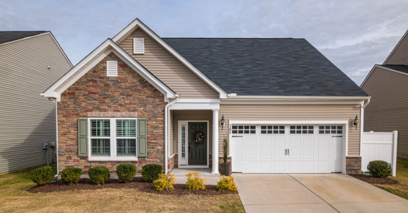 Exterior of house painted beige with white trim and garage doors and bushes outside.