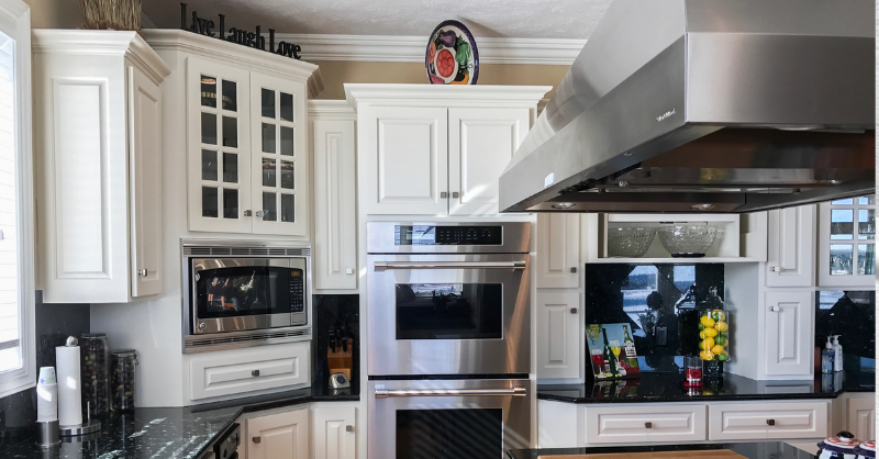 Kitchen with white cabinets and stainless steel appliances. Upper cabinets have decor pieces above them.