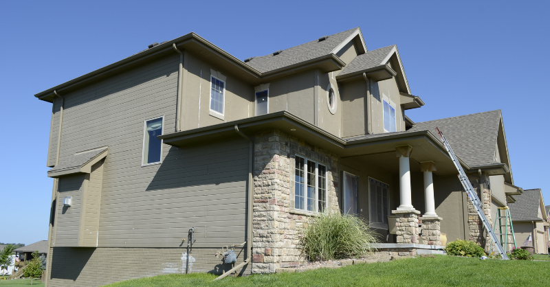 Exterior of home painted a light beige color with a ladder against the side.
