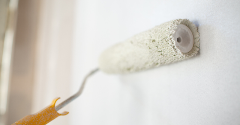 Paint roller painting wall white.