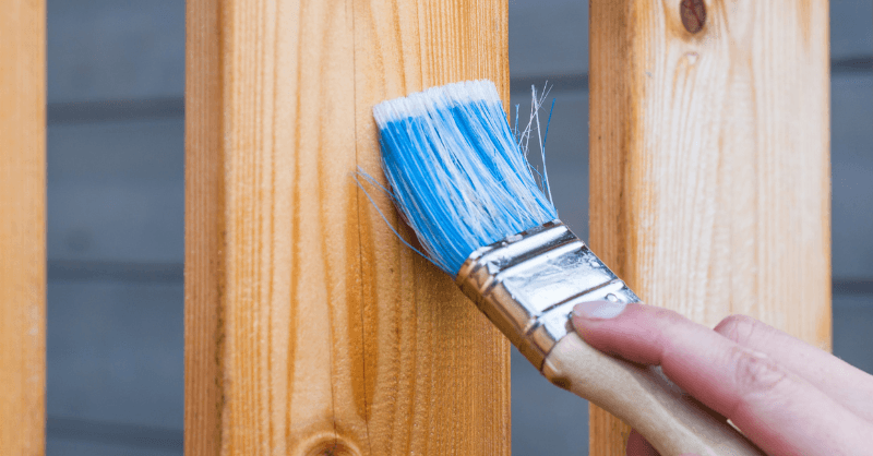 Painter staining railings on a wooden deck.