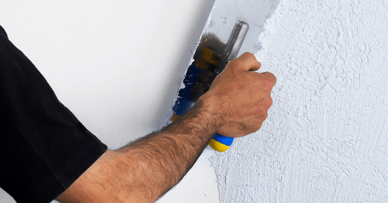 Painter plastering walls with plaster compound and a tool.