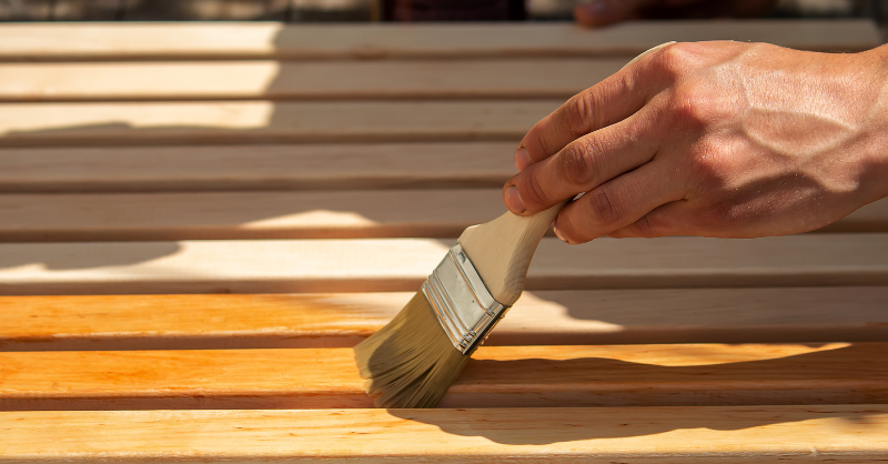 Painter varnishing wood furniture with a brush.