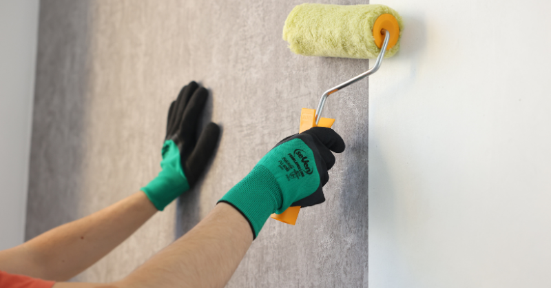 Painter installing peel and stick wallpaper on a white painted wall with a roller.