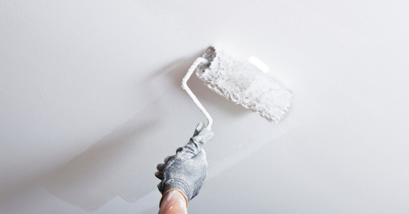 Persons hand with glove rolling white paint with a roller onto a ceiling.