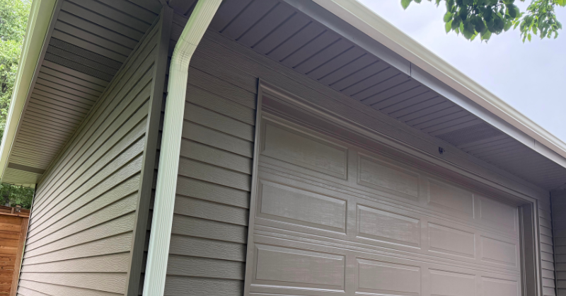 Exterior of a house freshly painted dark brown with a long white downspout extending from the side of the house.