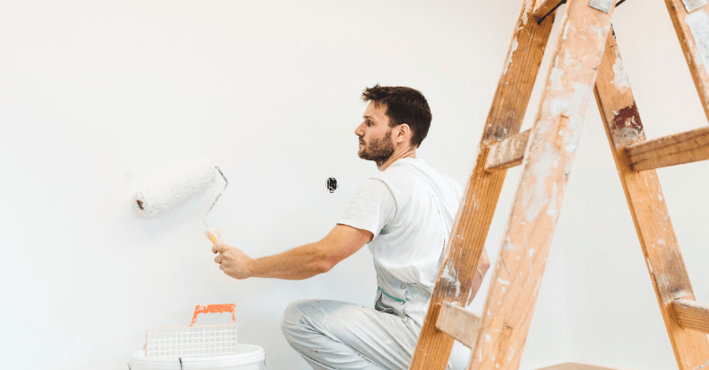 Local painter painting interior wall white with a roller.