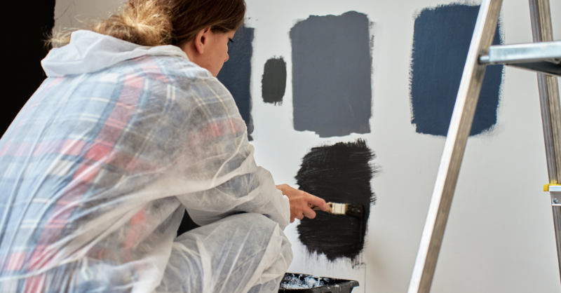 Woman painting dark black and blue paint swatches in squares on a white wall in Omaha, NE.