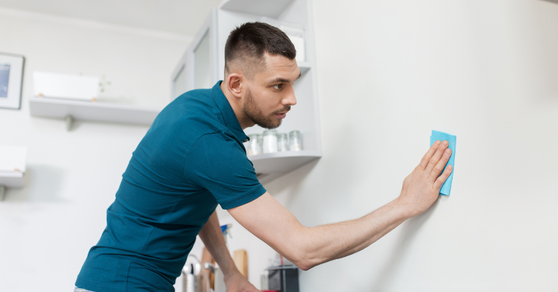Man scrubbing interior white wall with a sponge.