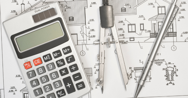 Plans of a house sitting on a desk with a calculator and pen.
