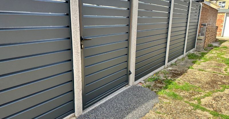 Black horizontal vinyl fence in a backyard with a door.