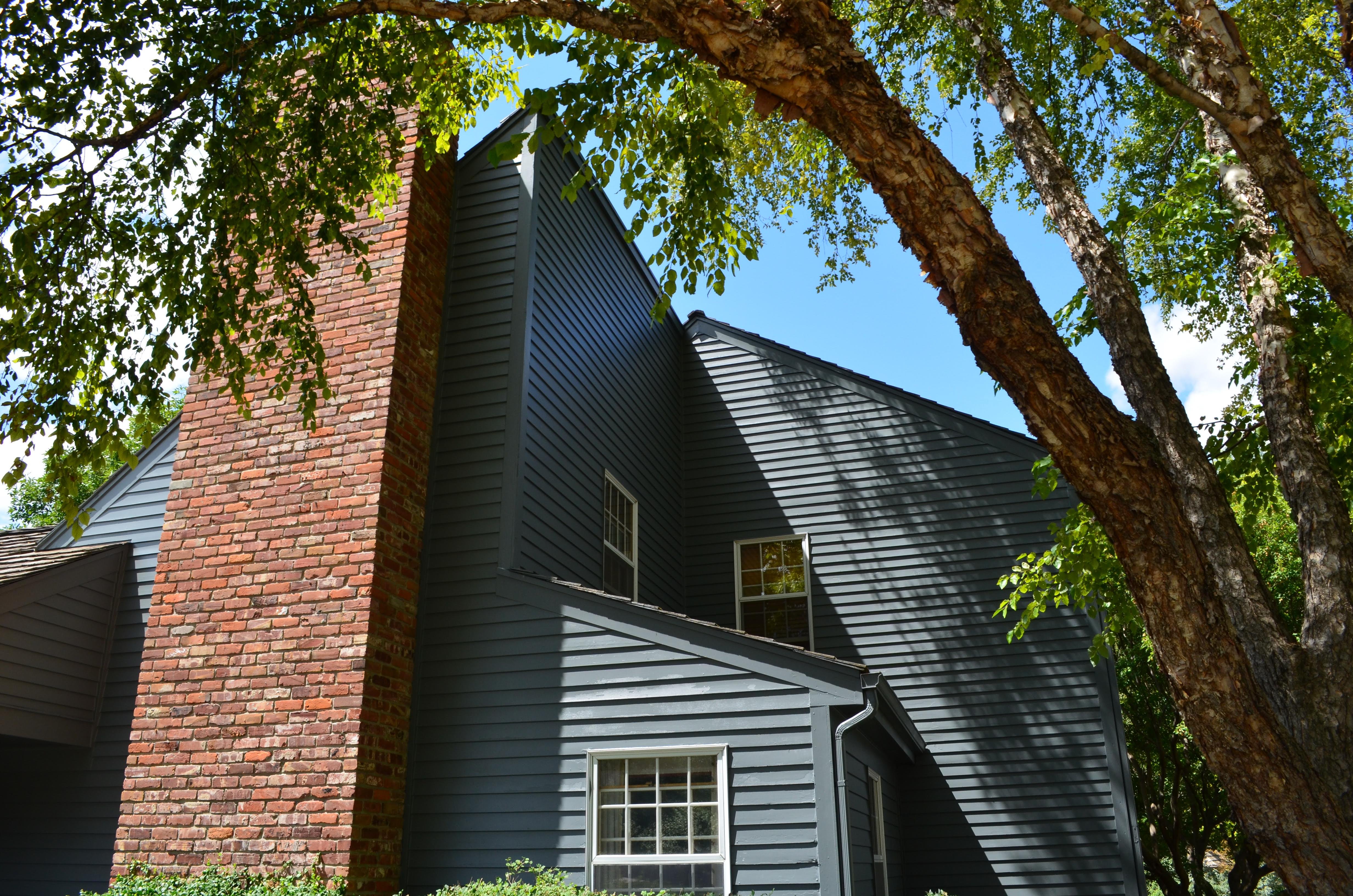 House painted a dark cool navy blue color with a large brick fireplace down the side and white trim.