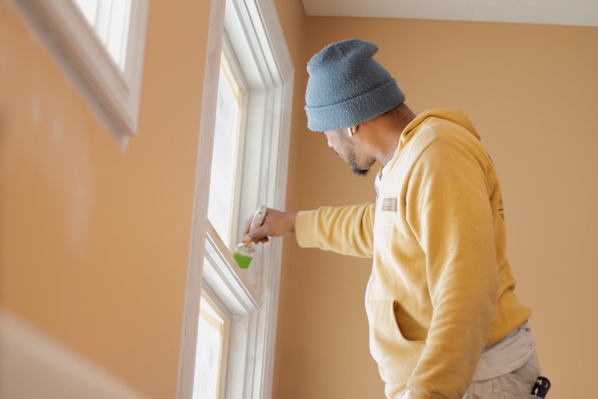 Painter brushing window trim with white paint.