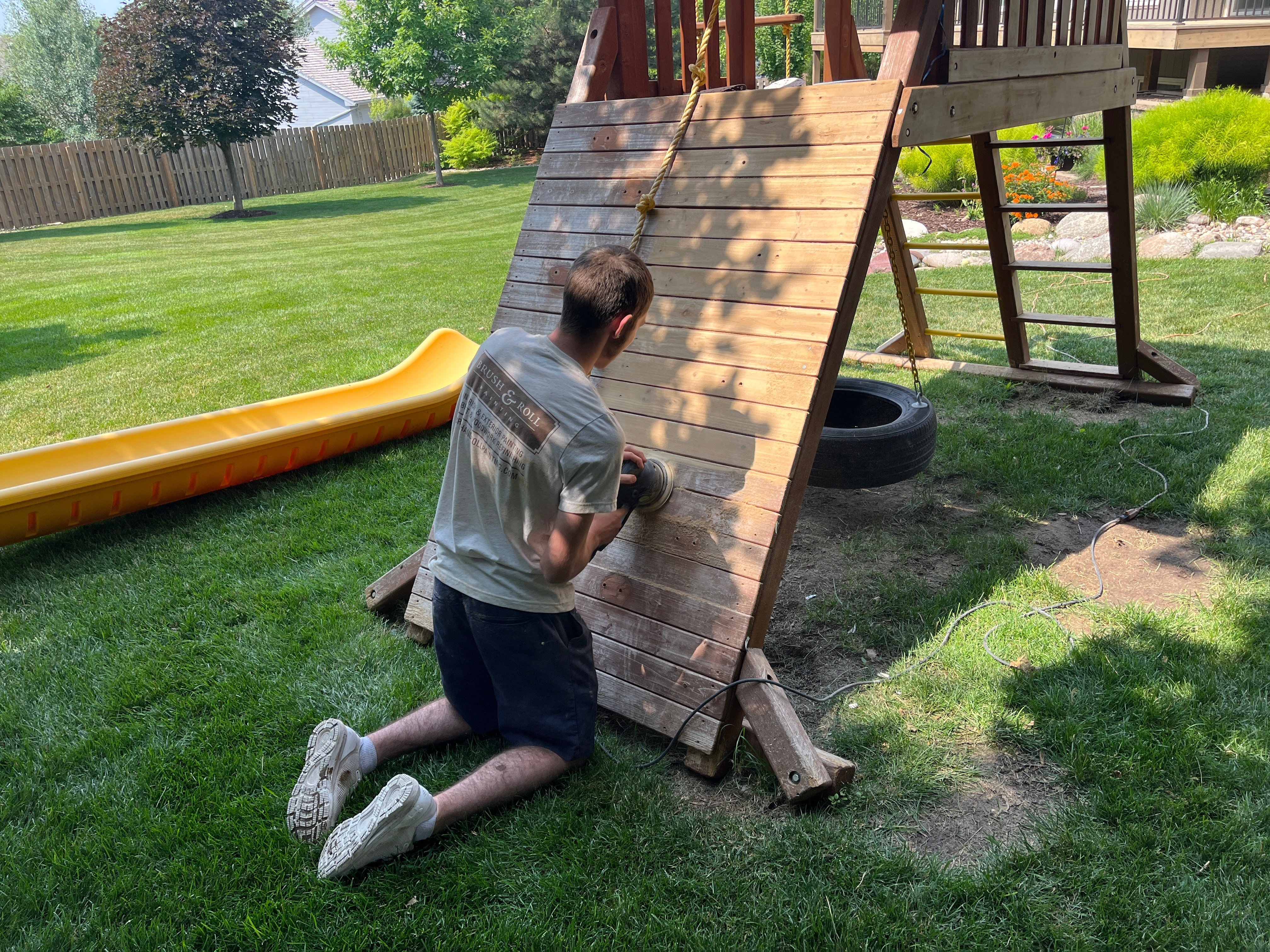 Painter sanding down rock climbing wall on a wooden playset outside of a home in Omaha, NE.