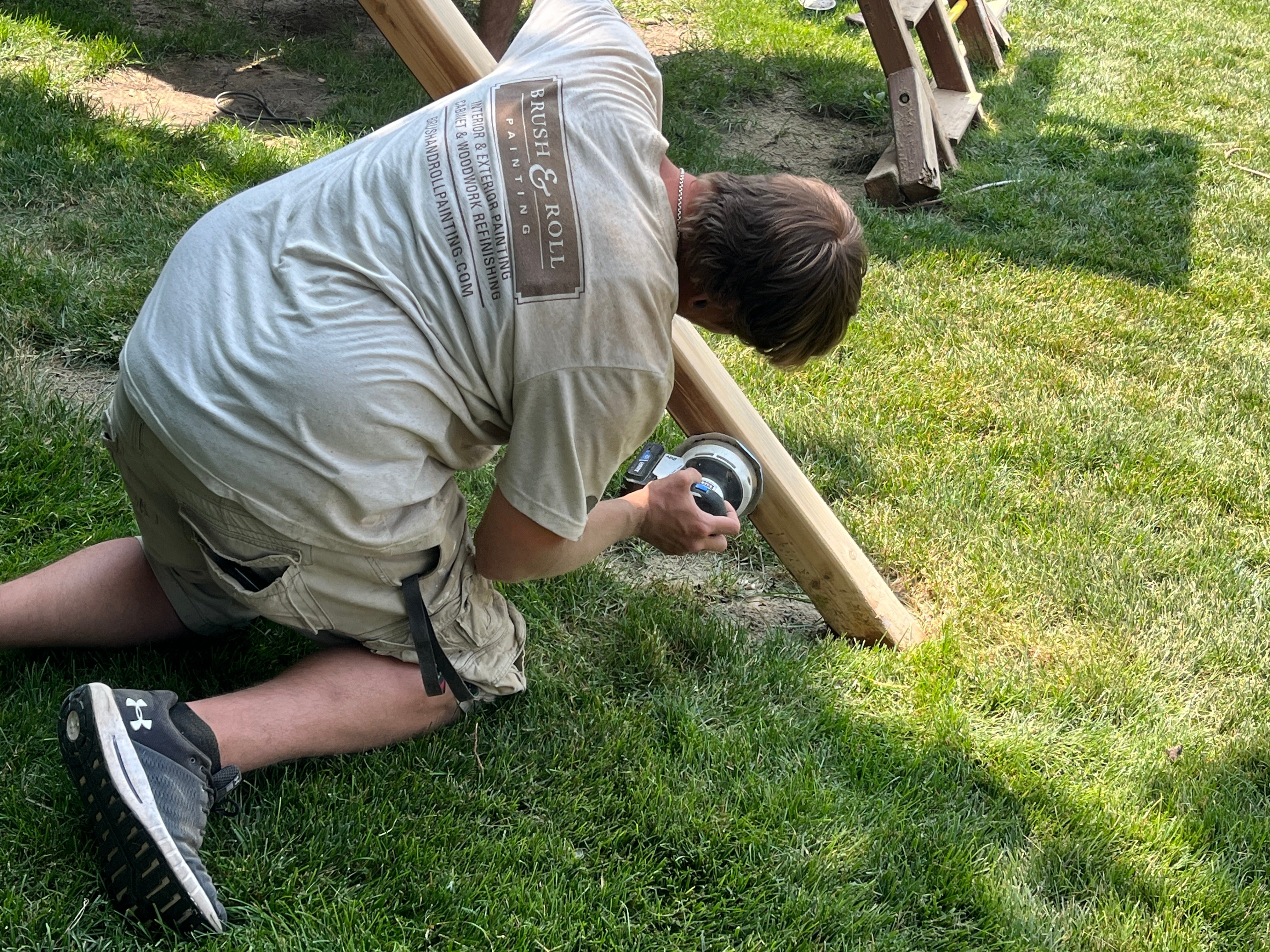 Brush & Roll Painting painter sanding off old finish on a wood playset before restaining in Omaha, NE.