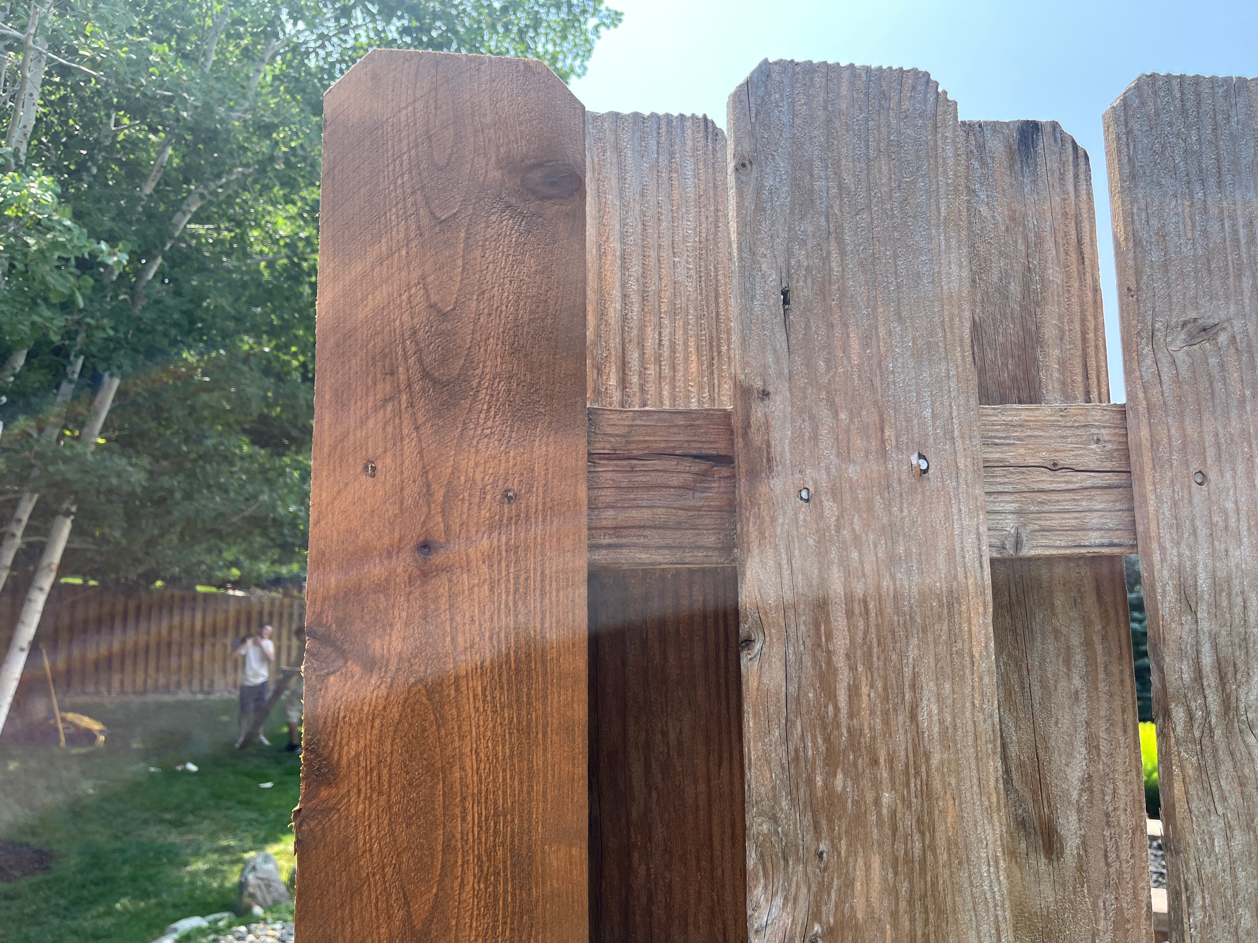 Fence posts showing one stained a warm light brown color and one unstained.