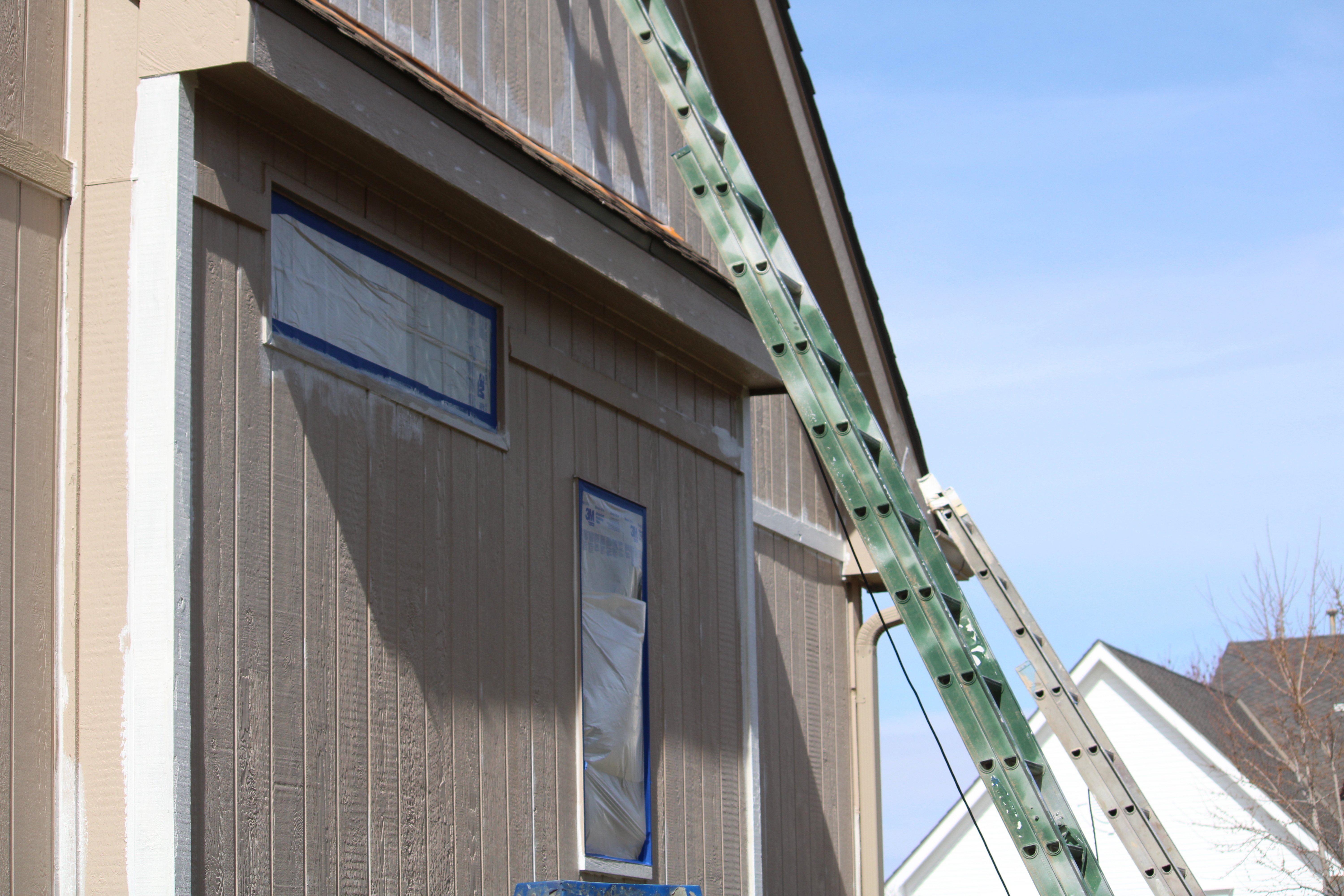 Side of a house in the process of being painted with ladders against the siding.