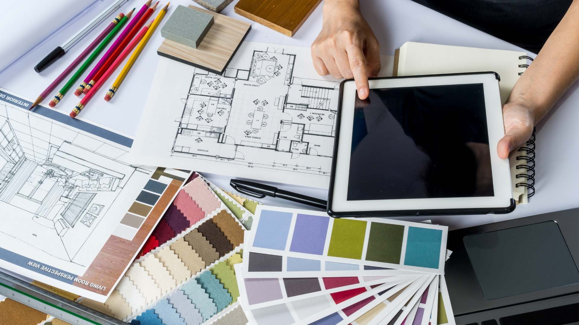 Person working on iPad with many color swatches and map of home laid out on table