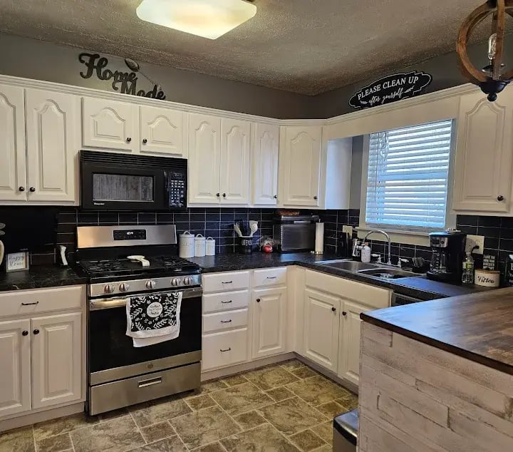 Kitchen with painted white cabinets, black countertops, and stainless steel appliances.