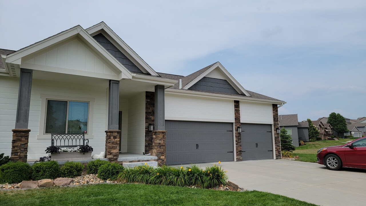 Exterior of home with siding painted white and garage doors and pillars painted grey with dark brick accents. Home in is Omaha, Nebraska.
