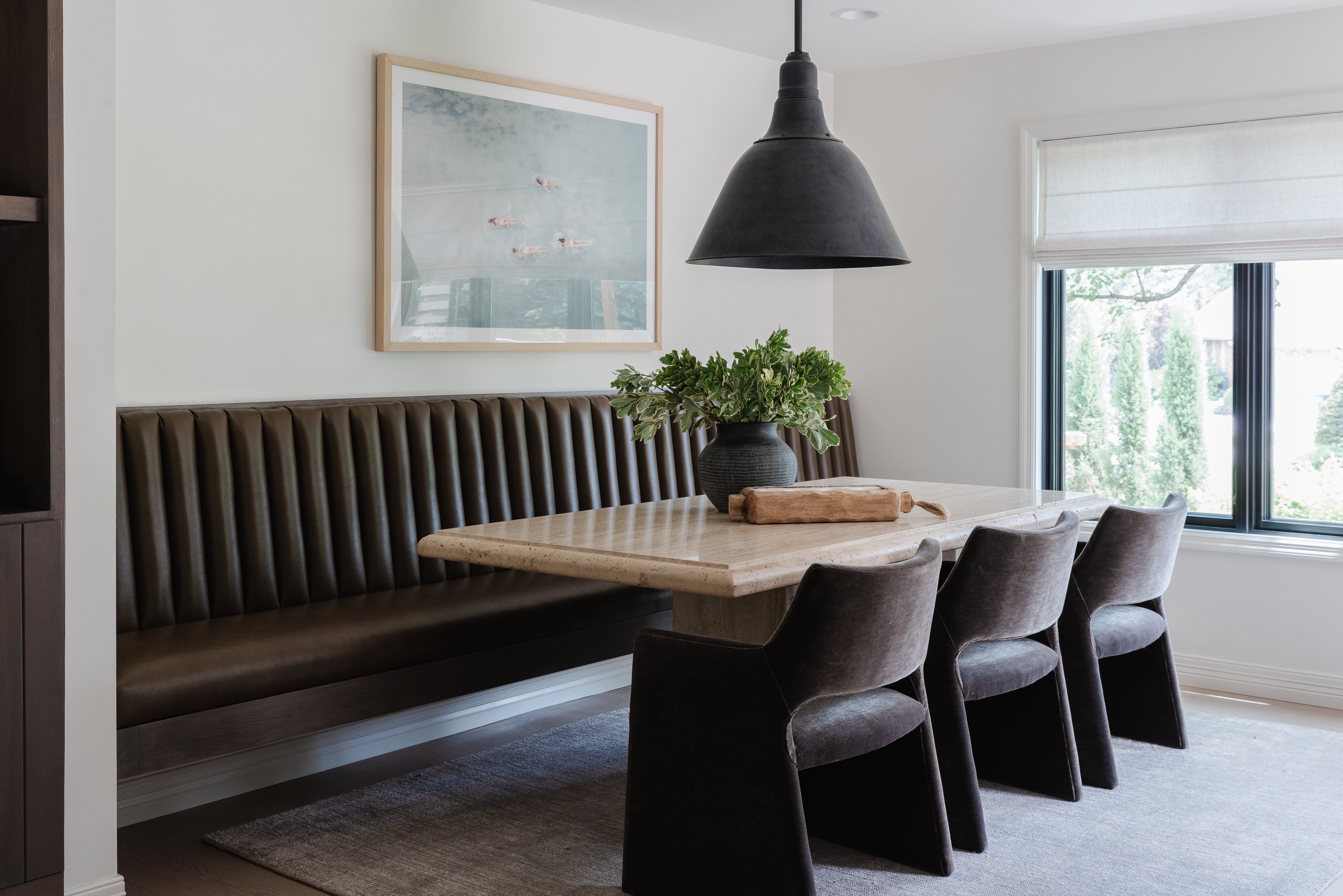 Dining room with black bench against white wall, warm colored table, and black chairs.