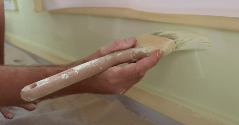 Painter brushing paint on to edges of baseboards and window sill