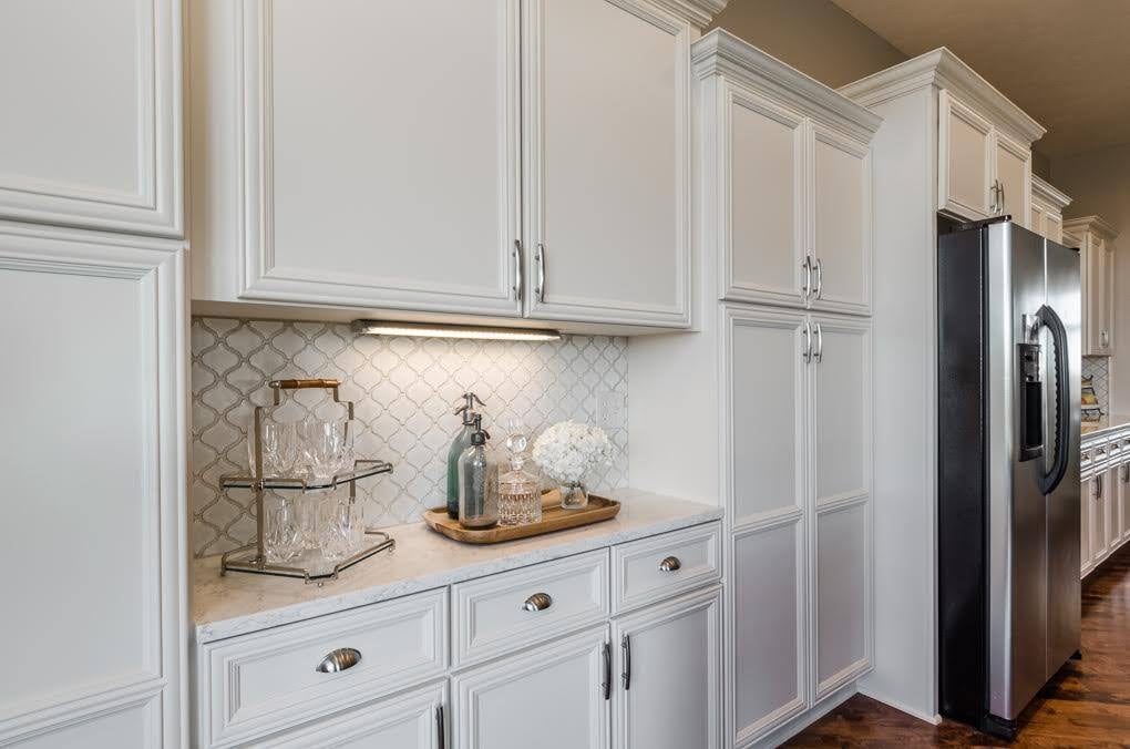 White painted cabinets with silver handles and white countertop and backsplash in a kitchen .