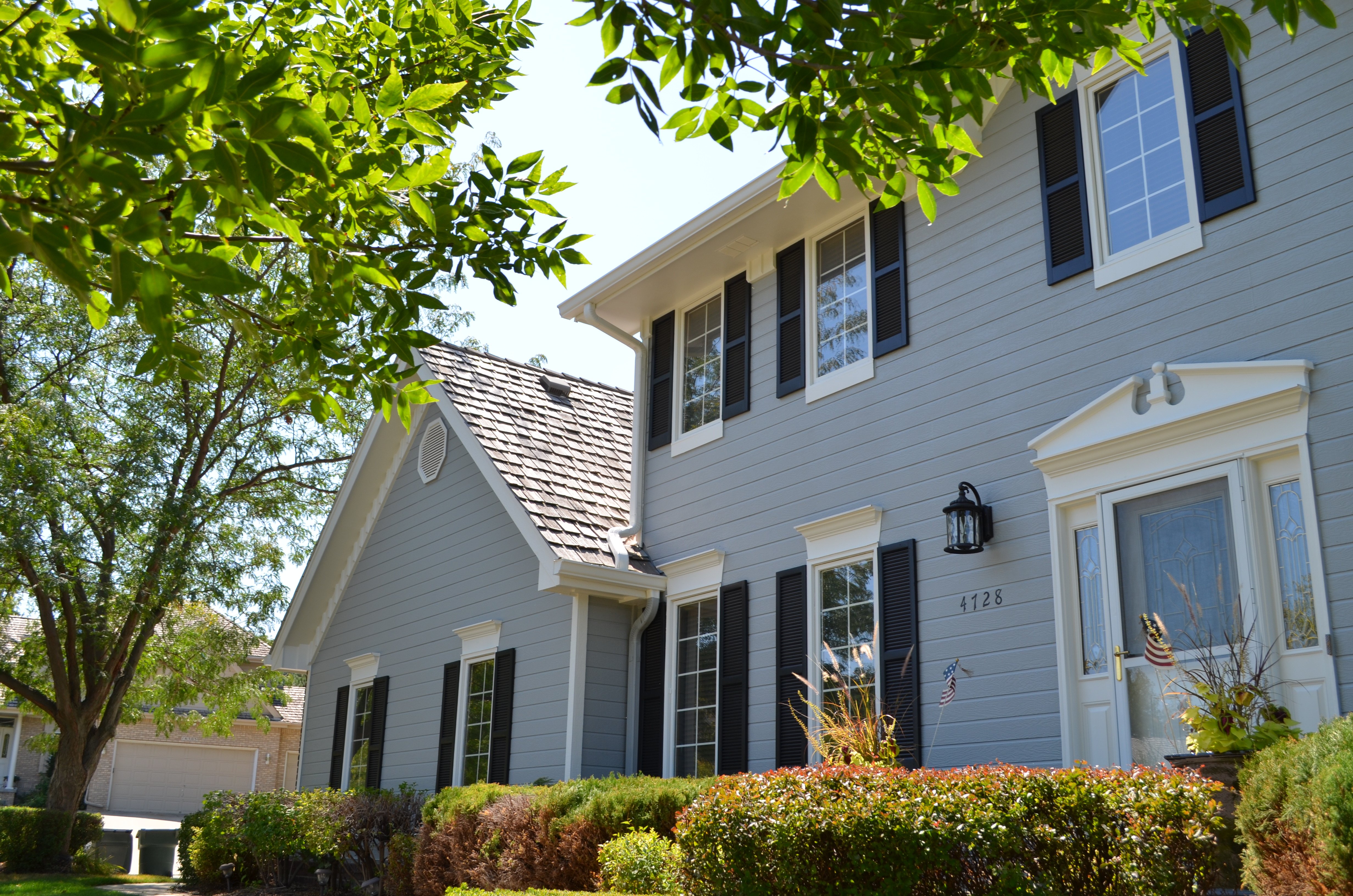 Front of exterior of home painted light blue with dark window shutters and white window and door trim.